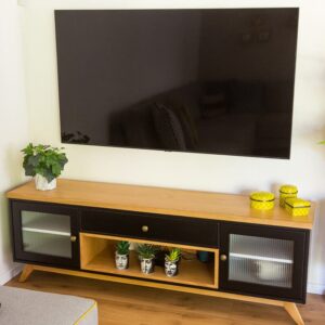 מזנון מעץ עם טלוויזיה תלויה, צמחים קטנים וקופסאות צבעוניות, תאורה נעימה לסלון.